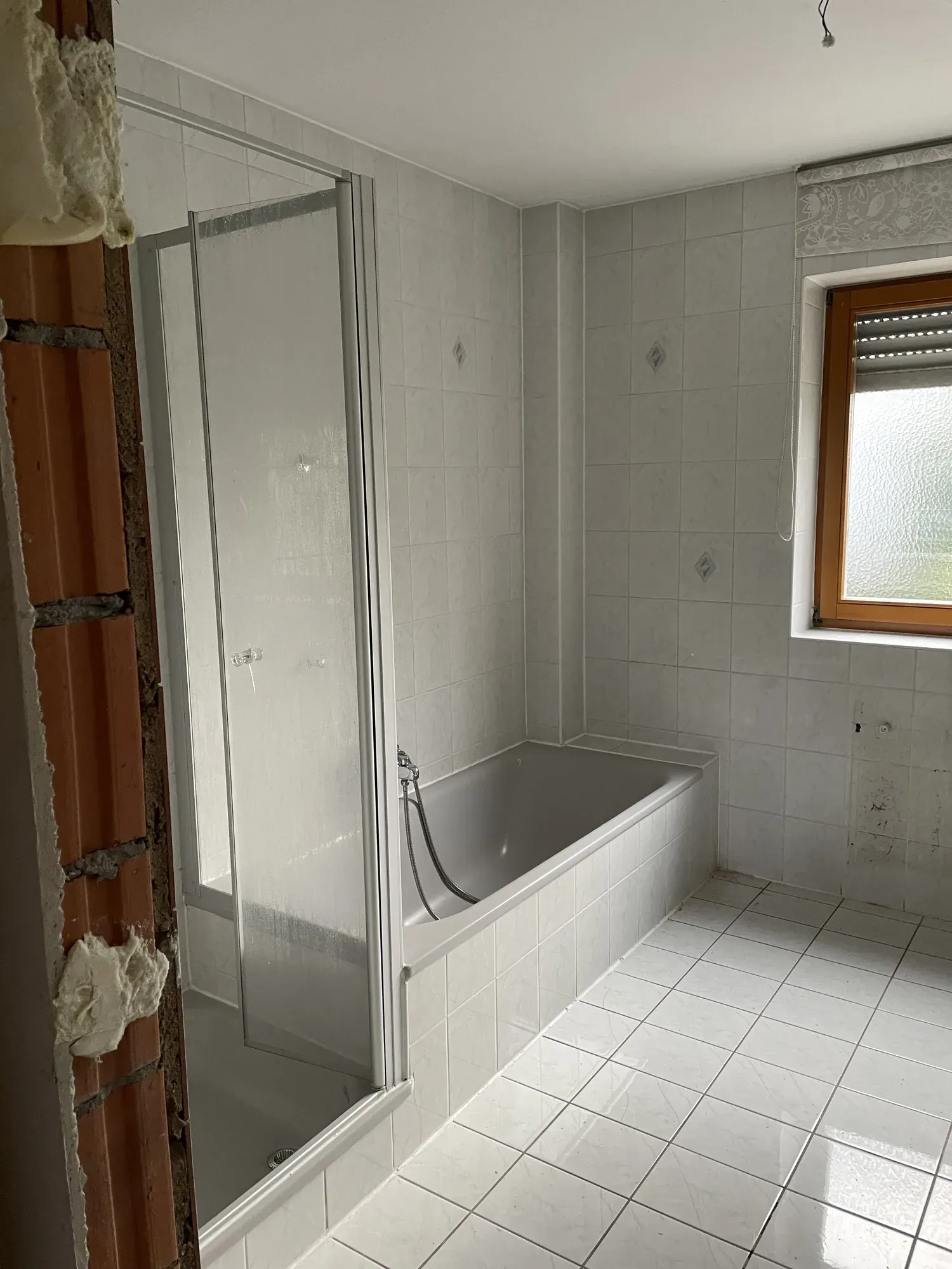 Altes Bad mit weißer Duschkabine und Badewanne vor dem Rückbau