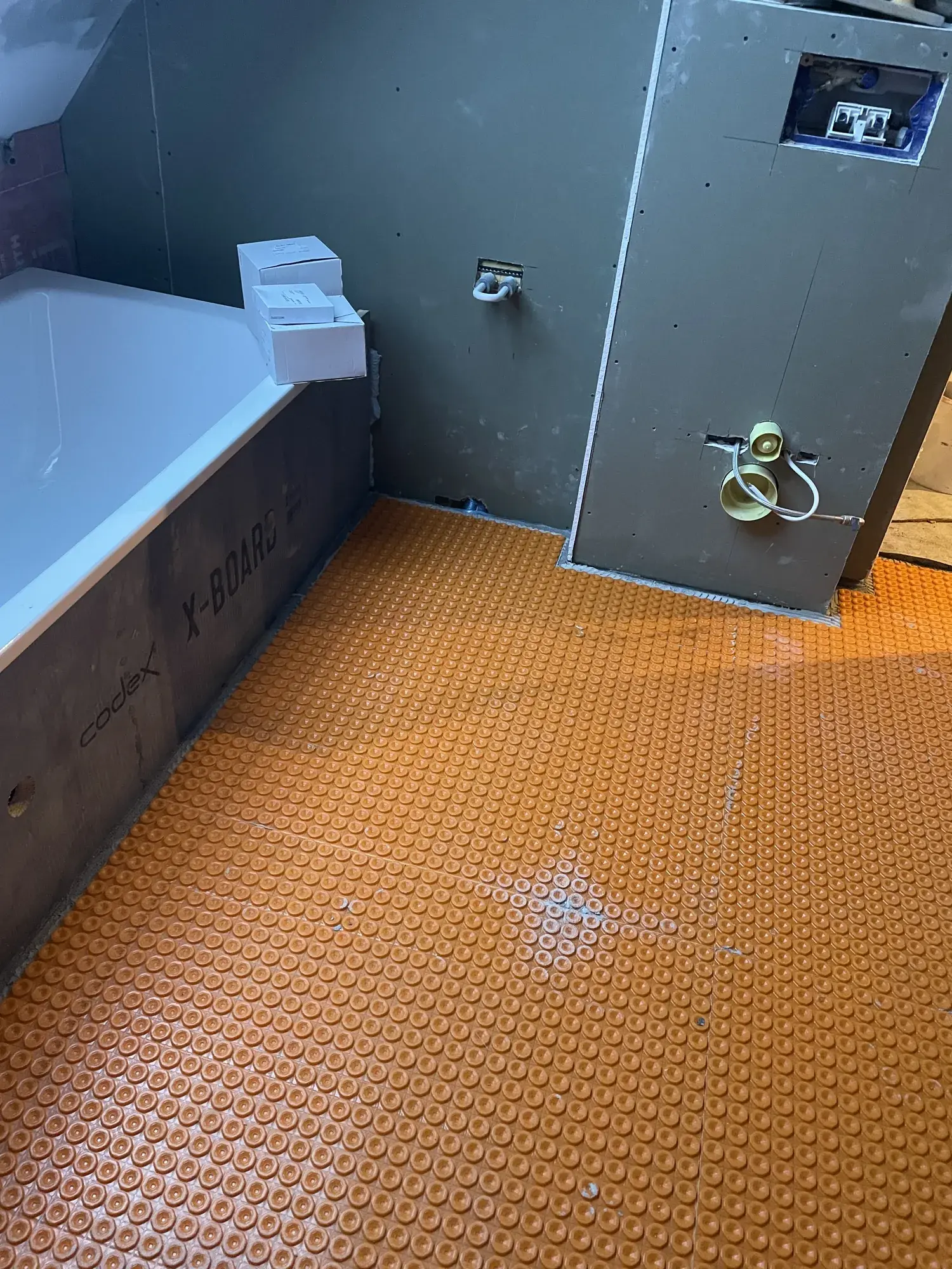 Zementgebundene Bauplatten an der Wand und orangefarbene Entkopplungsmatte auf dem Boden eines Bads vor dem Fliesen
