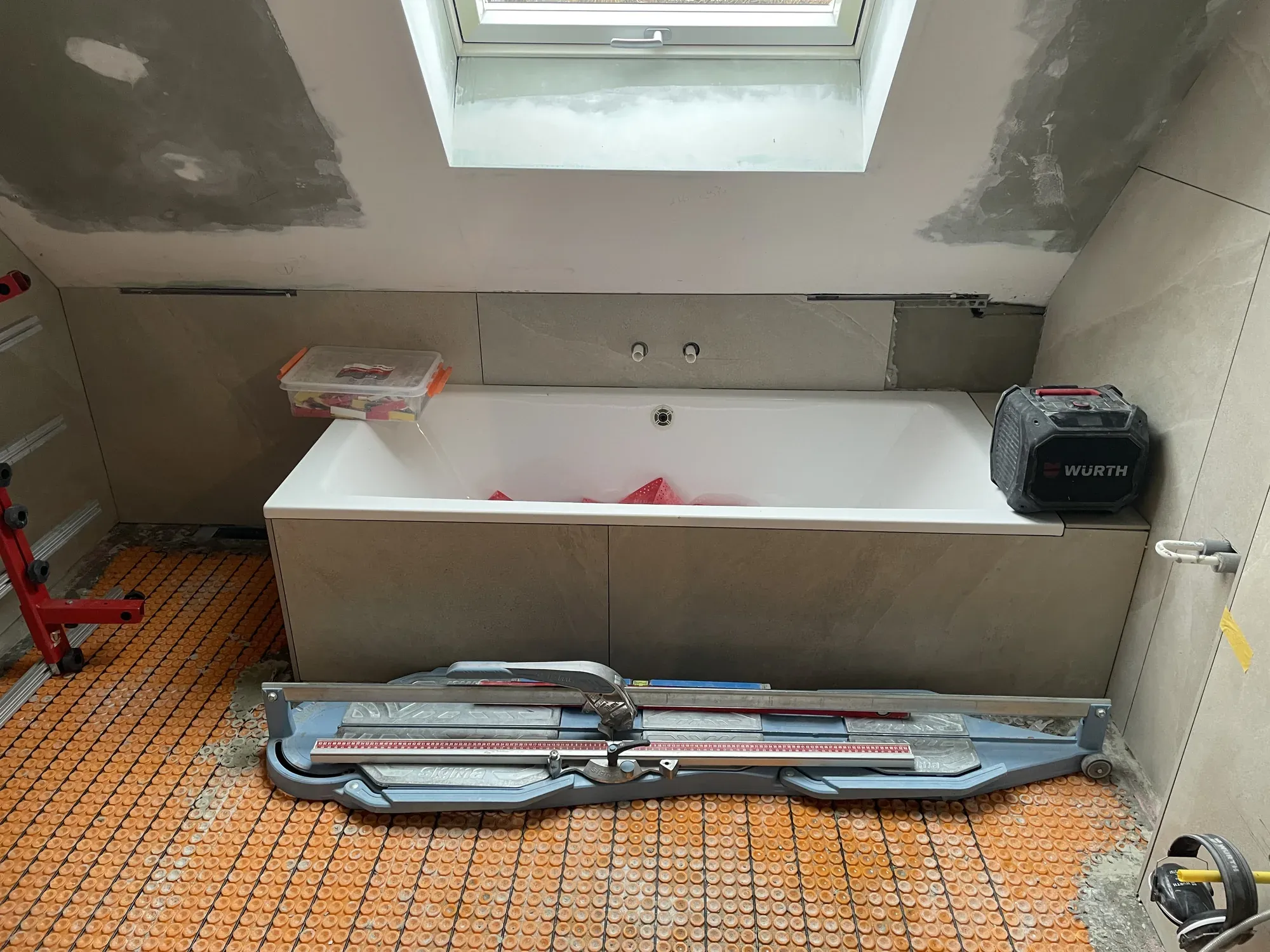 Badewanne wird mit sandfarbenen Großformatfliesen verkleidet, Werkzeug auf dem Boden